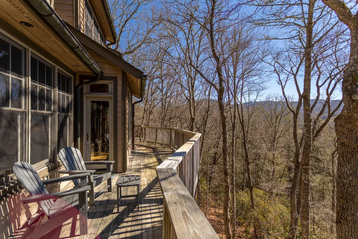 A spacious wooden deck furnished with Adirondack chairs, overlooking a sweeping mountain vista and surrounded by trees. The deck invites morning relaxation or evening gatherings in the fresh air.