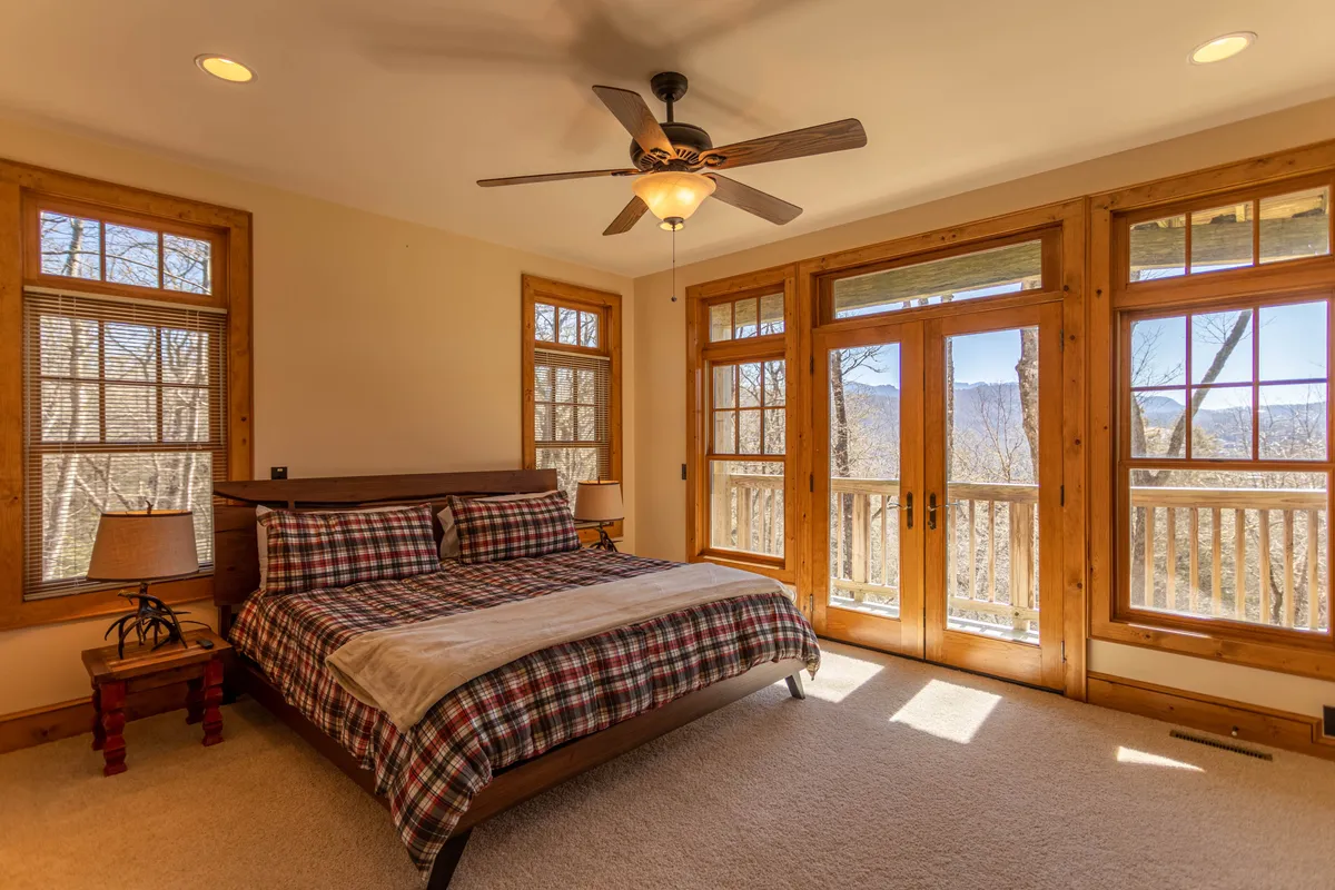 A tranquil bedroom featuring a bed positioned near large windows overlooking natural scenery, complemented by wooden furniture. The open view through the windows suggests a direct connection to the outdoors, ideal for beginning or ending a day of adventure.