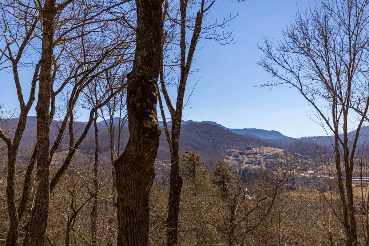 A sweeping mountain vista with bare trees in the foreground and a clear blue sky overhead. The image evokes a sense of adventure and the stunning natural environment that surrounds Banner Elk.