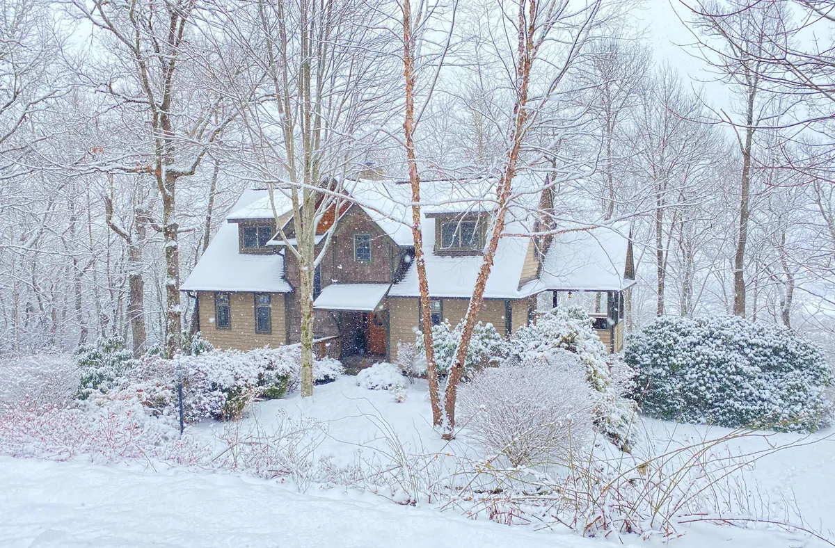The house nestled in a snowy landscape, surrounded by trees and exuding a cozy, tranquil vibe. The wintry setting speaks to seasonal charm and the variety of experiences available year-round.