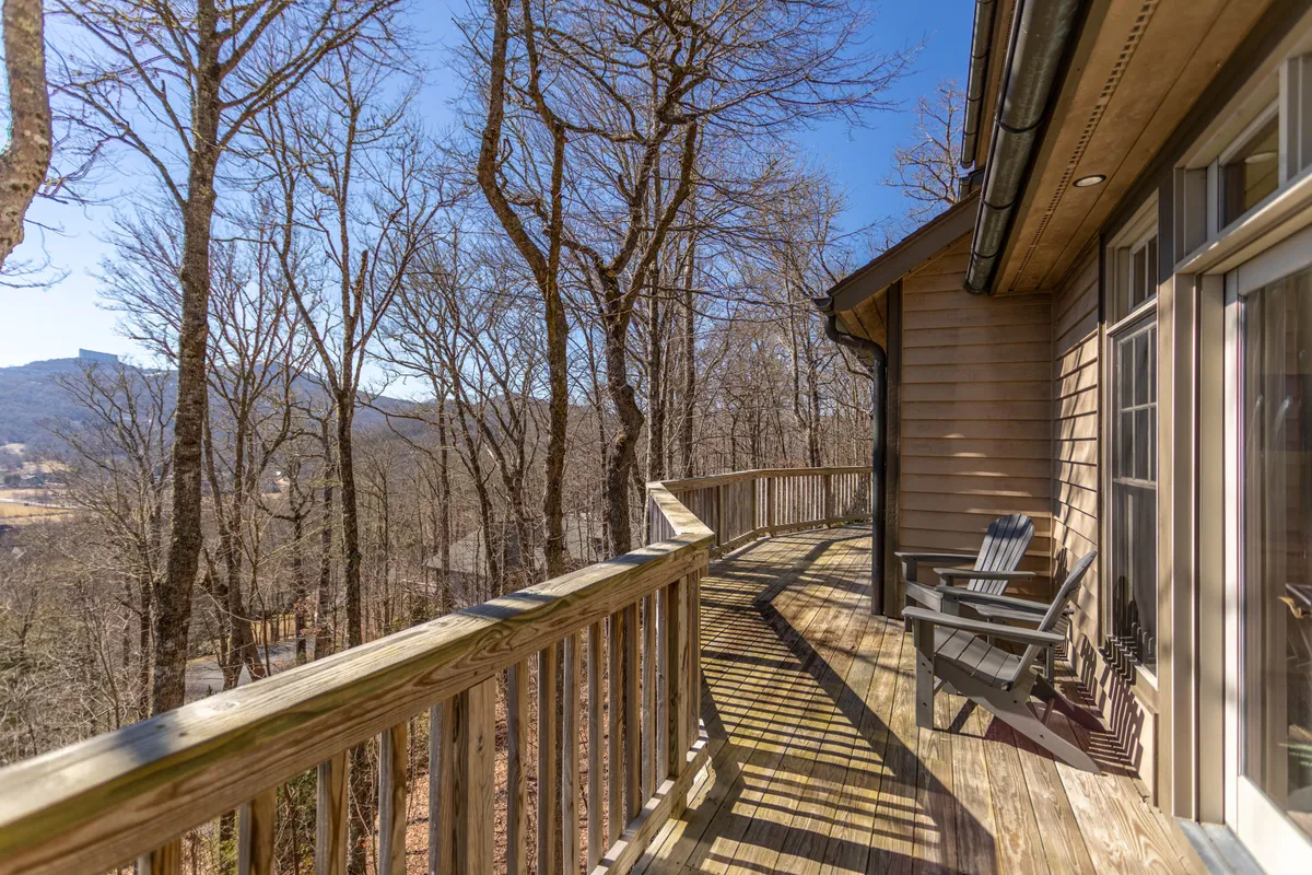 This image displays a spacious wooden deck surrounded by mature trees and overlooking a picturesque mountain view. The deck is an inviting space for guests to relax outdoors and enjoy the natural setting with their pets.