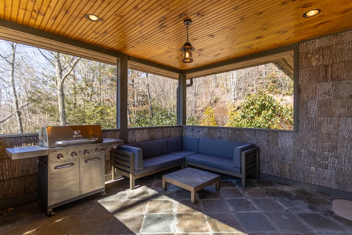 This image captures an inviting outdoor grilling area with a stone grill, wooden ceiling, and comfortable seating, surrounded by natural landscape. The setting is casual and perfect for social gatherings or quiet relaxation, directly reflecting the community's outdoor amenities.