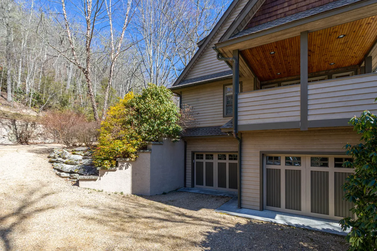 A welcoming view of the house’s exterior framed by a landscaped pathway, surrounded by lush trees. The setting is tranquil and hints at the natural beauty and accessibility of the area. The porch offers a relaxing spot to watch sunsets or gather before heading into town.