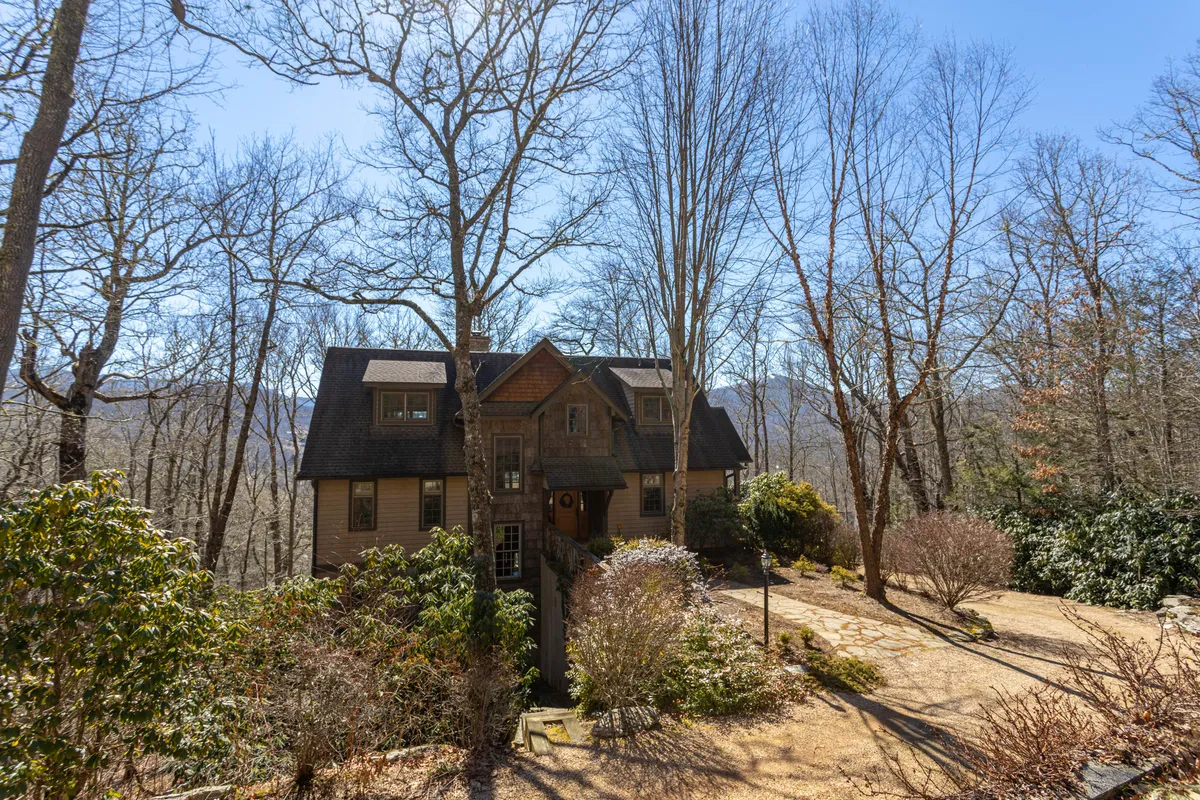 A wide exterior shot showing the house framed by lush trees, with a pathway that invites leisurely strolls. The natural, tranquil setting highlights the community’s scenic walking paths and connection to nature.