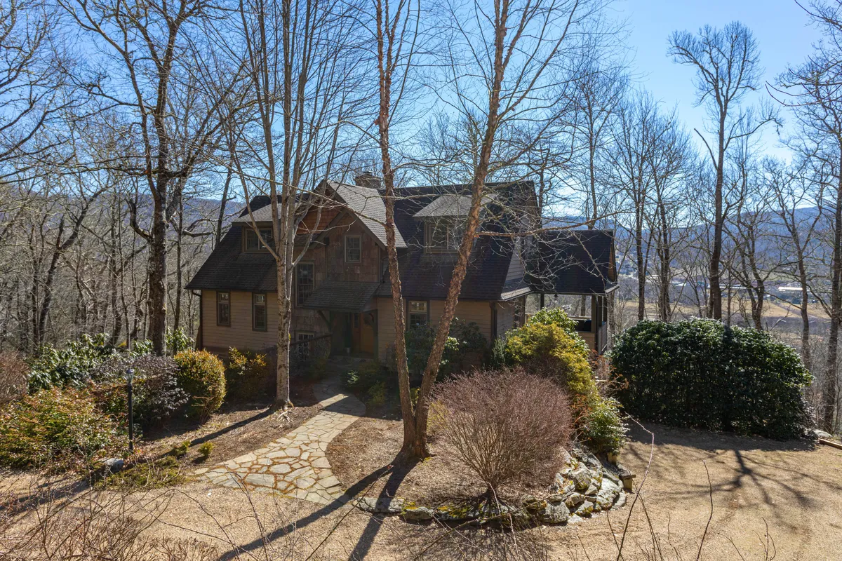 A peaceful exterior view of the house featuring a stone pathway and lush surrounding trees and shrubs. The setting suggests tranquil nature walks and plenty of green space—all welcoming for guests with dogs.